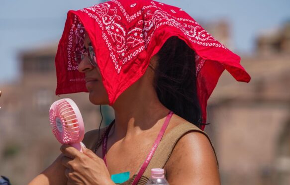 A woman with a portable fan covers her head from the soaring heat.